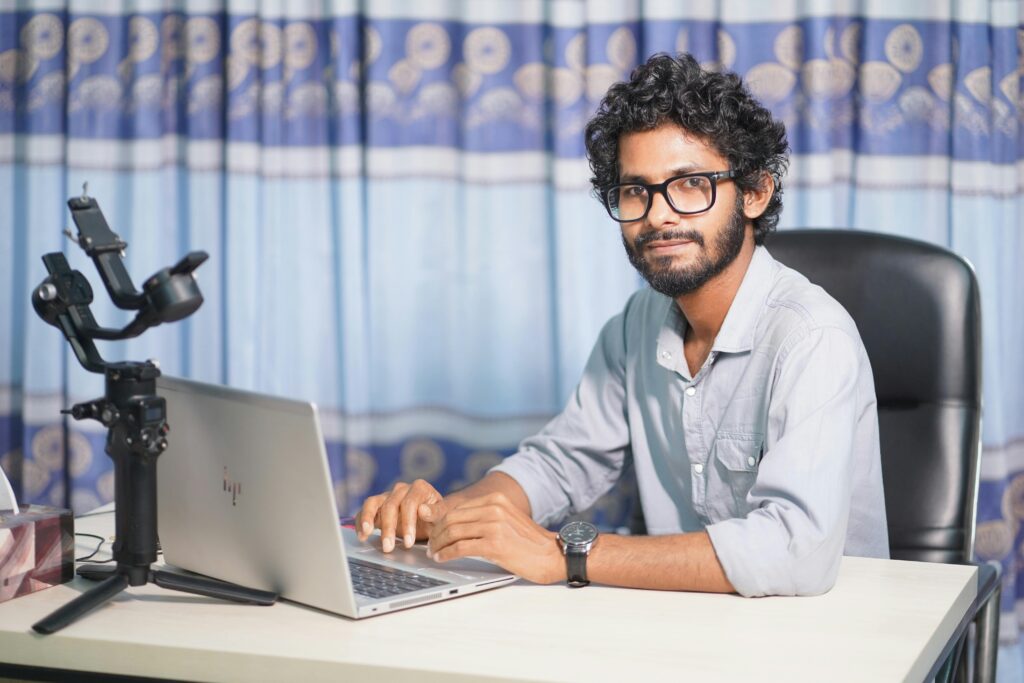 Portrait of a web developer with a laptop and camera, working at his office desk in a modern setup.