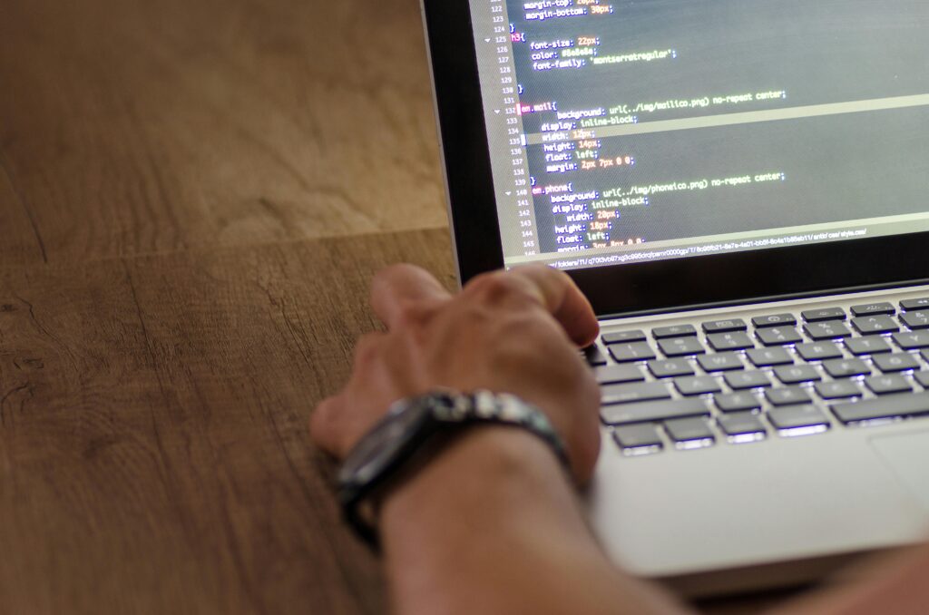 A developer's hand interacting with code on a laptop screen in a workspace setting.